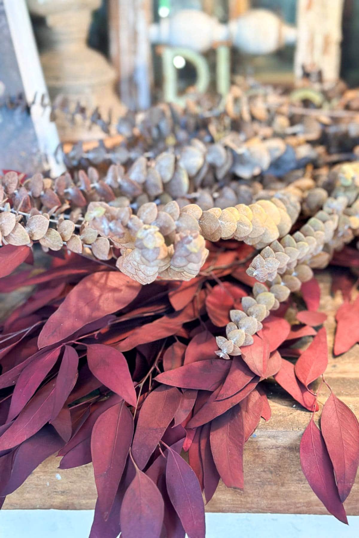 A close-up of a flower arrangement featuring earthy tones. The arrangement includes dried brown clusters resembling berries and dried reddish-brown leaves. The background is slightly blurred, highlighting the textures of the plants.