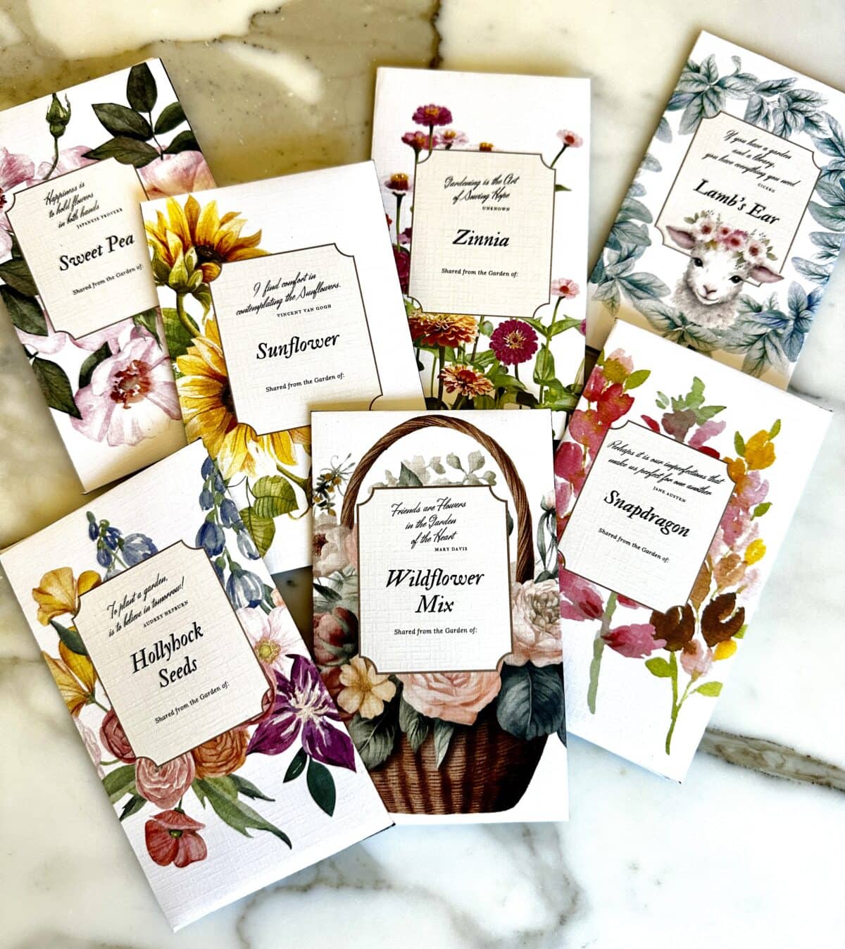 Seven packets of flower seeds displayed on a marble surface. The packets include Sweet Pea, Sunflower, Zinnia, Lamb's Ear, Snapdragon, Hollyhock Seeds, and Wildflower Mix, each adorned with colorful illustrations of the respective flowers. Perfect for participating in a seed exchange.