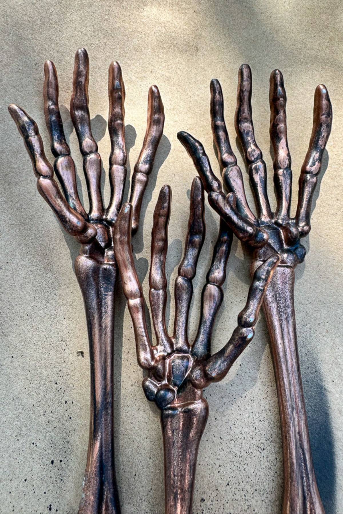 Three bronze-colored skeletal hands with elongated fingers are displayed on a flat surface, perfect for adding a spooky touch to your Halloween table. Their metallic sheen and detailed joint structures offer an eye-catching addition to your Halloween decorations, exuding a slightly weathered appearance.