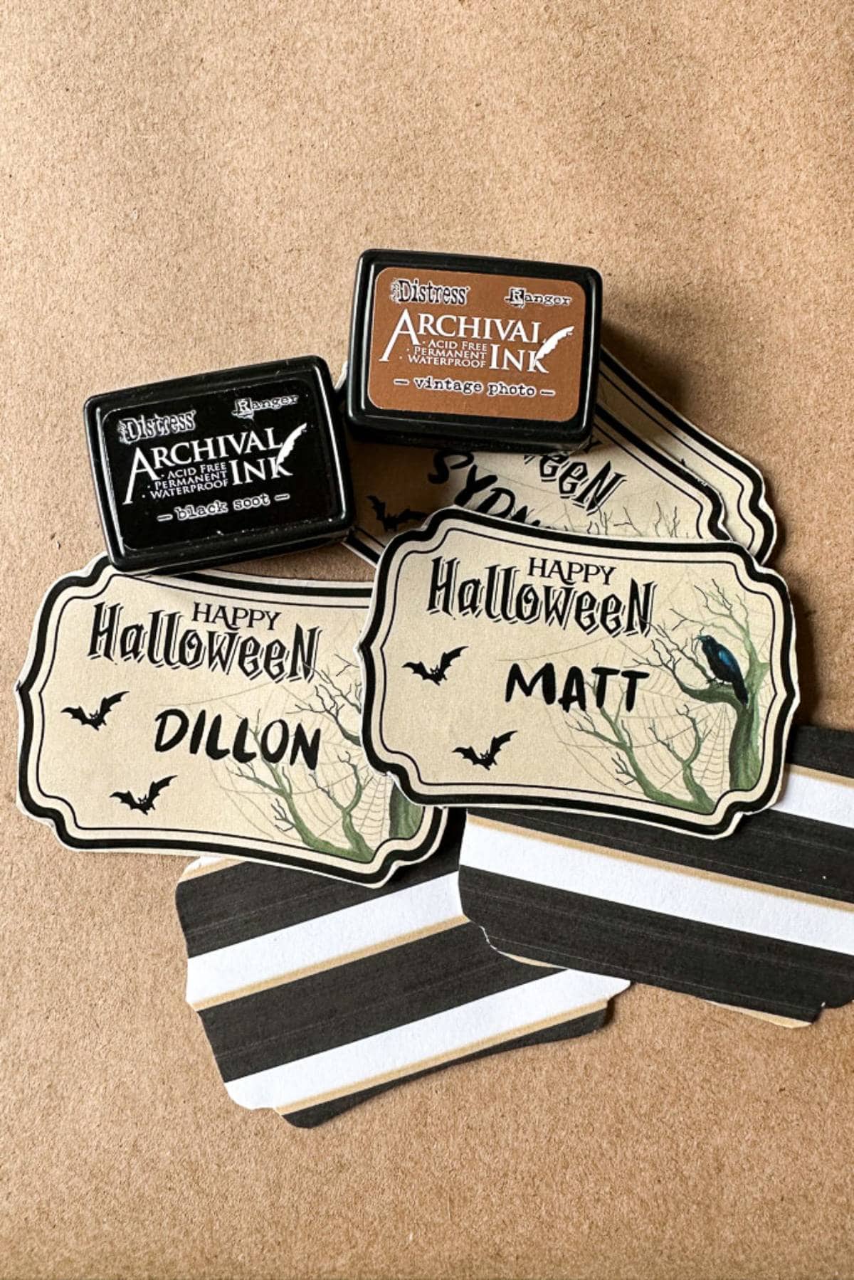 Two "Happy Halloween" cards with the names "Dillon" and "Matt," surrounded by blank cards with tree and bat designs. On top are two small Archival Ink containers, one in black (Jet Black) and one in brown (Vintage Photo), both for stamping.