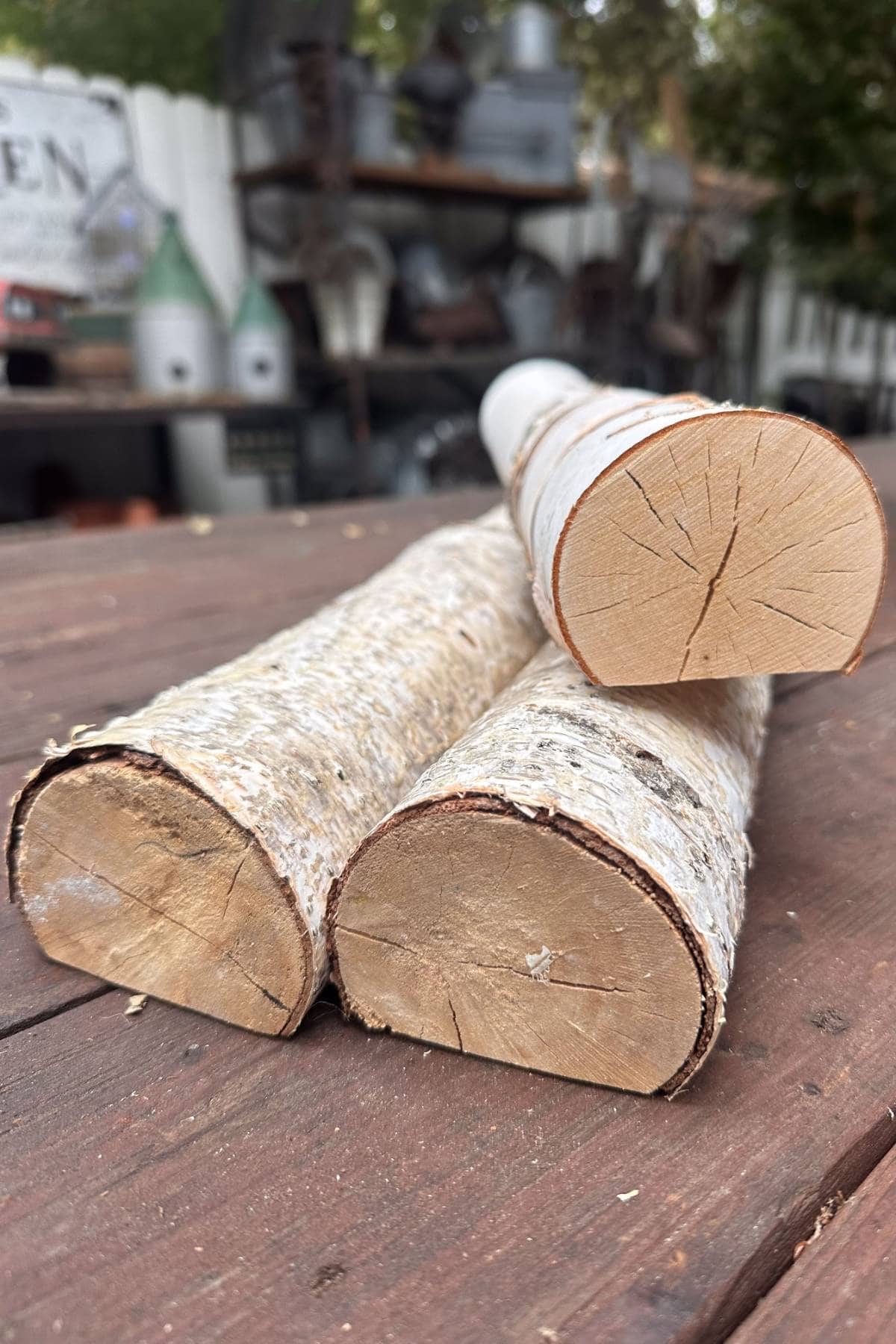 Three birch logs stacked on a wooden surface against a rustic background.