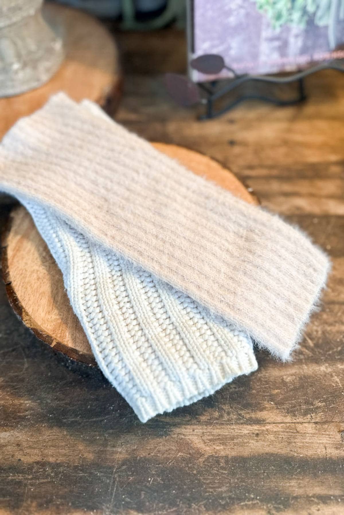 Two folded knitted scarves rest on a wooden surface. One scarf is light gray and fuzzy, while the other is white with a ribbed texture. They are arranged neatly and appear cozy and warm.