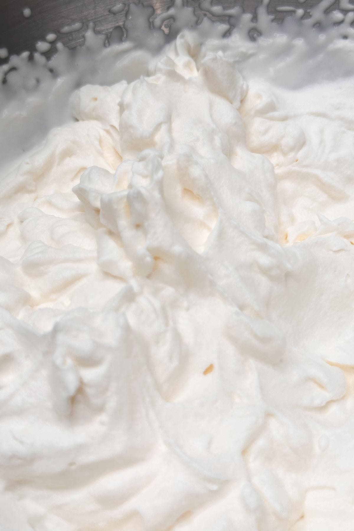 Close-up of whipped cream, showcasing its smooth, fluffy texture and soft peaks. The cream is white and fills the entire image, highlighting its airy and light appearance.