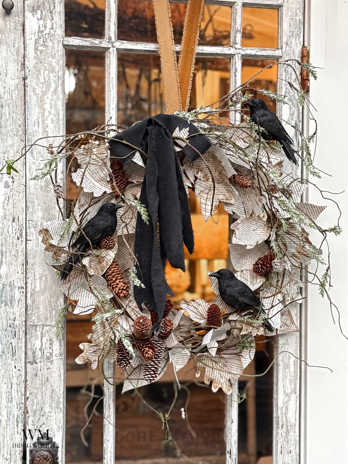 A rustic wreath with pinecones, artificial leaves, twigs, black ribbon, and three black bird decorations hangs on a weathered glass door, an ideal piece of DIY Halloween decor that adds a touch of eerie charm to your entryway.