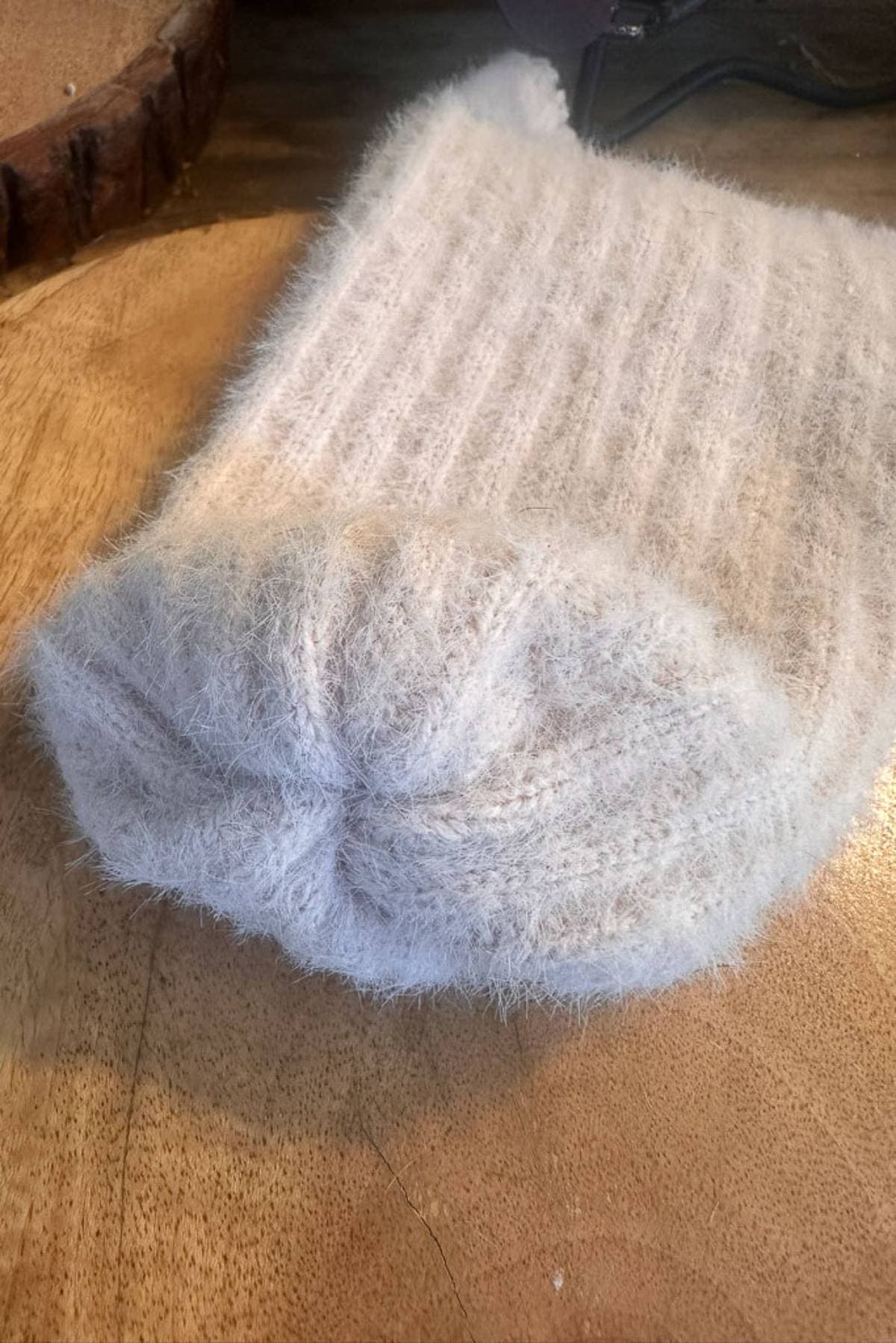 A soft sweater sleeve turned right side out after securing the end. Displayed on a wooden surface. The texture is fuzzy, giving a cozy appearance.