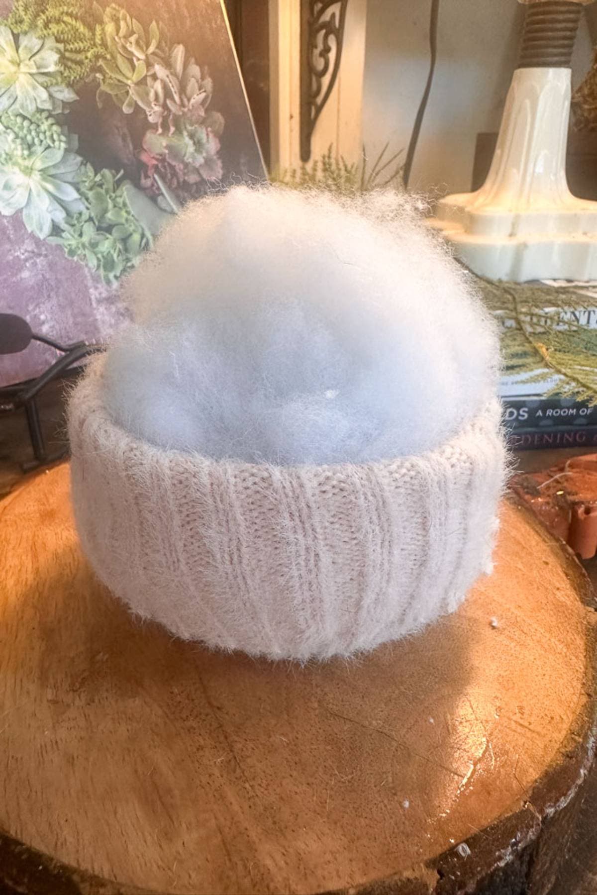 A fluffy sweater sleeve getting stuffed to create a sweater pumpkin sits on a wooden surface. In the background, there's a lamp and a book with plant images.