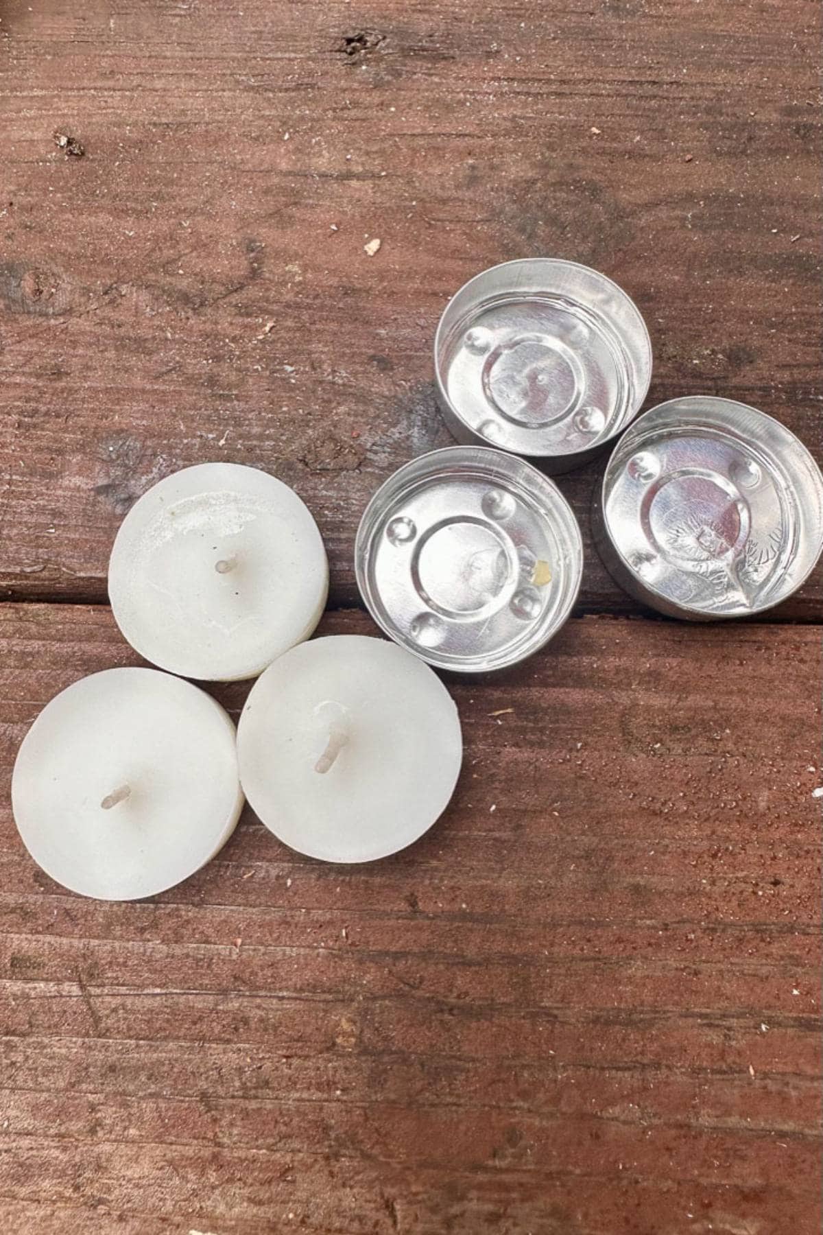 Four used tealight candles on a wooden surface. Three have no wax left, revealing the metal containers, and the fourth still has some wax remaining.