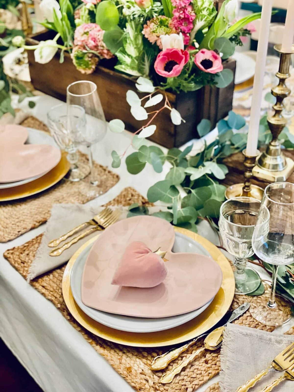 A beautifully set dining table features pink heart-shaped plates, gold cutlery, woven placemats, wine glasses, and a vibrant floral centerpiece—use a DIY template to easily recreate this romantic, elegant atmosphere at home.