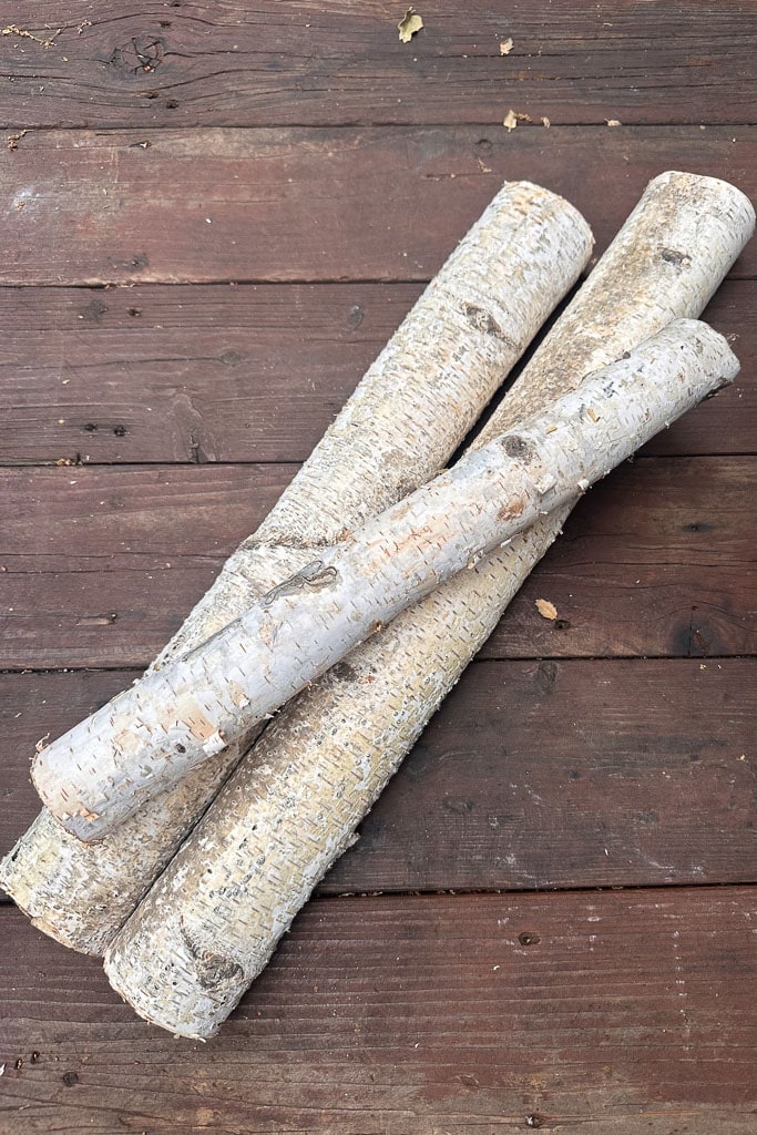 Three long birch logs with light bark rest on a wooden surface, their texture adding a rustic and natural look to the composition. Perfect for crafting DIY candle holders that bring warmth and charm to any space.