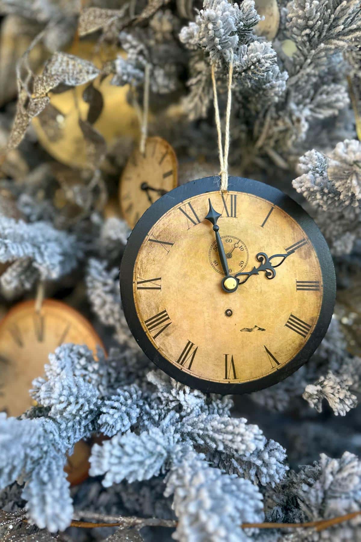 A vintage-style clock with Roman numerals hangs from a snow-dusted evergreen branch, surrounded by similar clocks. The clock hands are set at 10:10, creating a whimsical, wintry scene.