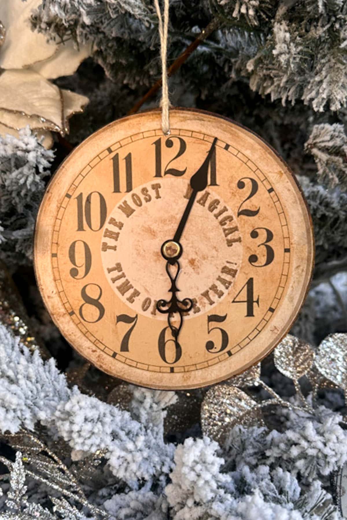 A DIY vintage Christmas ornament, featuring a round decorative clock with classic numerals, hangs on the snow-covered tree. The clock hands point to 11:55, and it reads "The Most Magical Time of Year," capturing the essence of festive nostalgia.