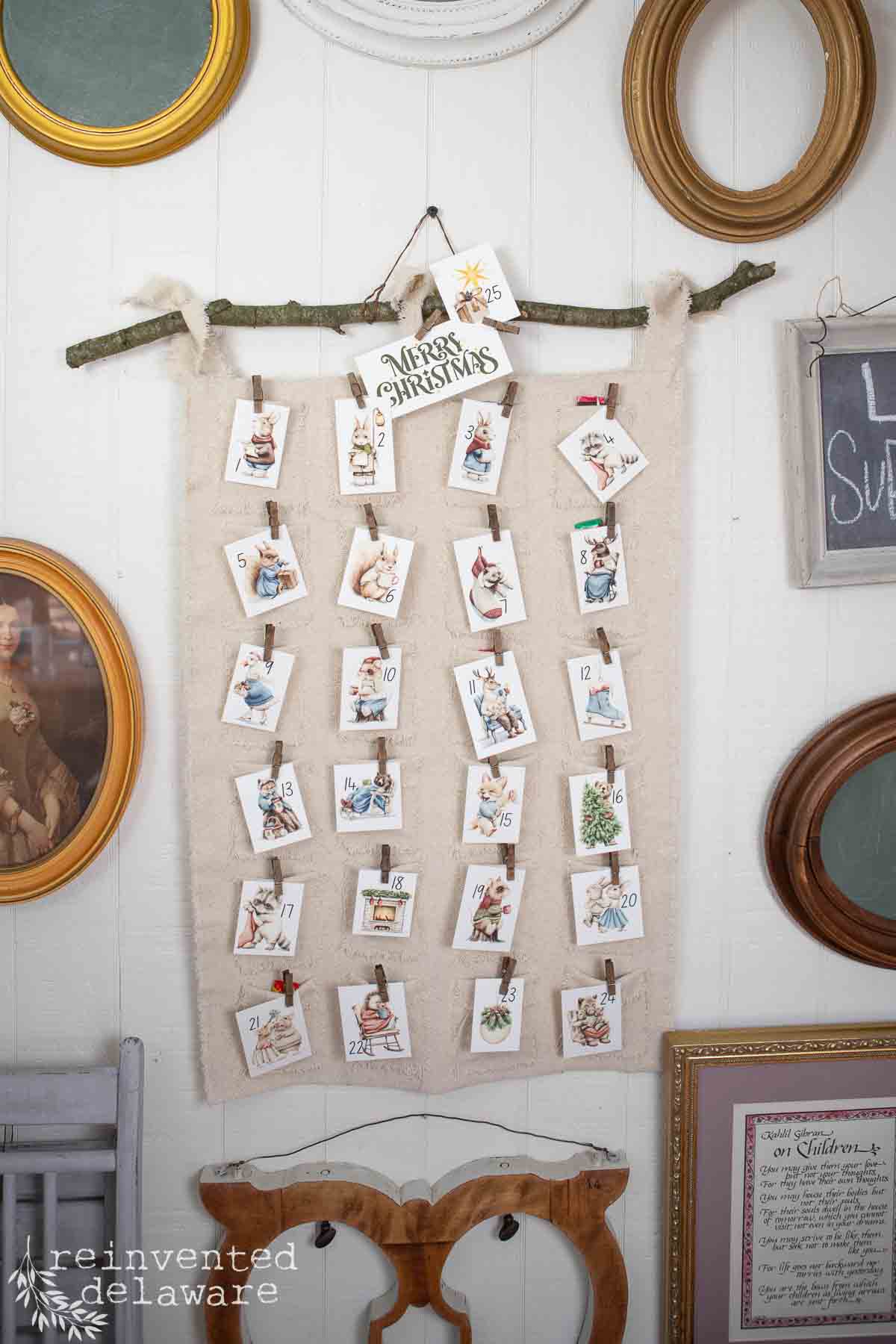 A handmade advent calendar hangs on a wall, featuring small cards clipped to twine with numbers and vintage Christmas illustrations. It exudes rustic charm, surrounded by empty picture frames and a small sign that reads "Merry Christmas," perfect decor for a cozy Christmas pajama party.