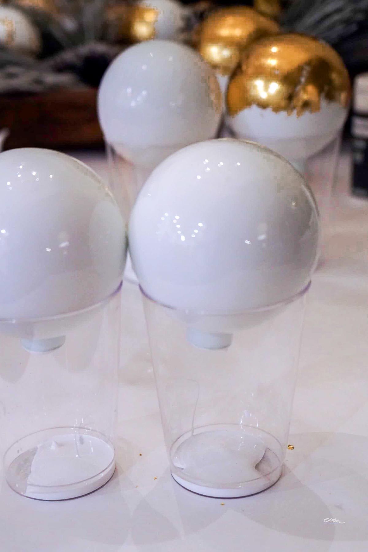 A collection of white and gold Christmas ornaments are placed on top of clear plastic cups, drying or being displayed on a table.