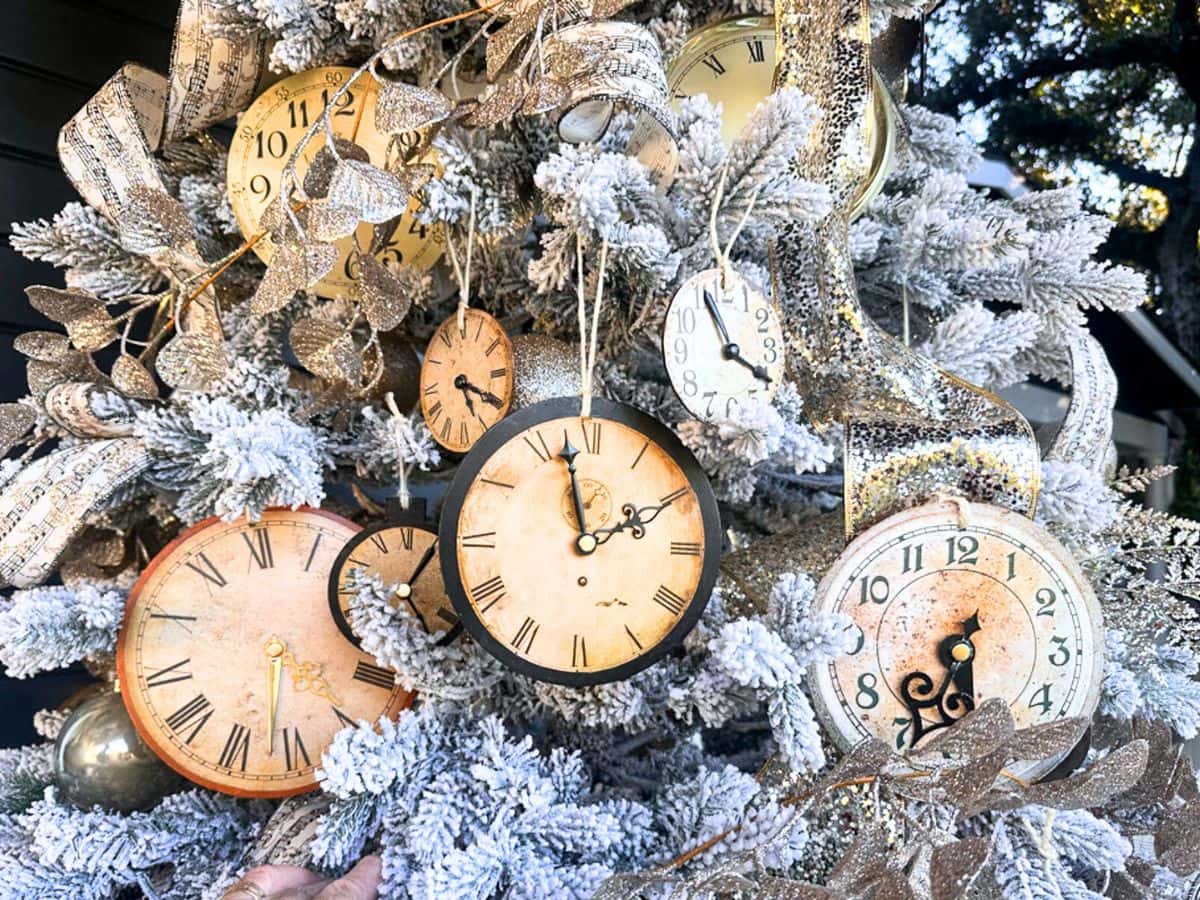 A Christmas tree adorned with DIY vintage clock ornaments, each displaying different times. The tree is frosted with white snow-like detailing and embellished with golden leaves and ribbons, creating an elegant, festive atmosphere.