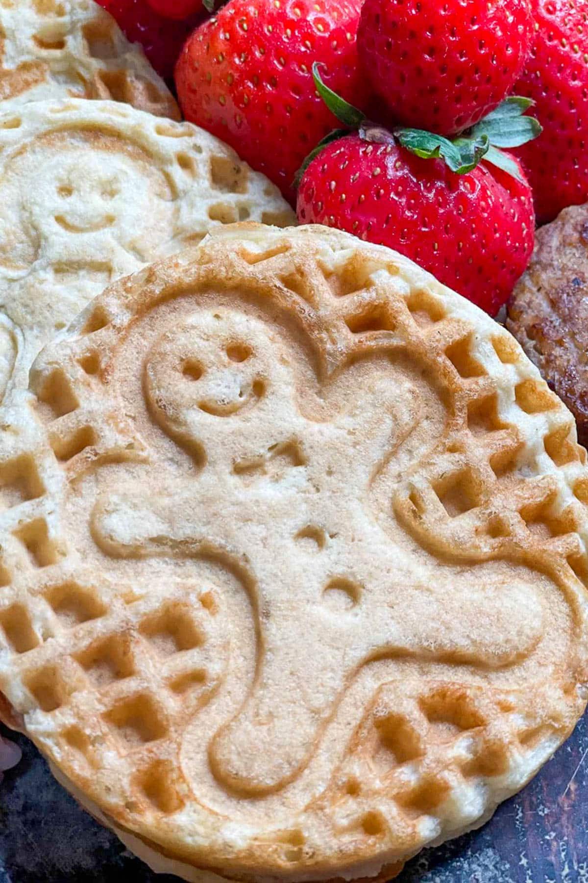 A close-up of a waffle with a smiling gingerbread man imprint, surrounded by fresh strawberries—perfect for a Christmas pajama party breakfast delight.