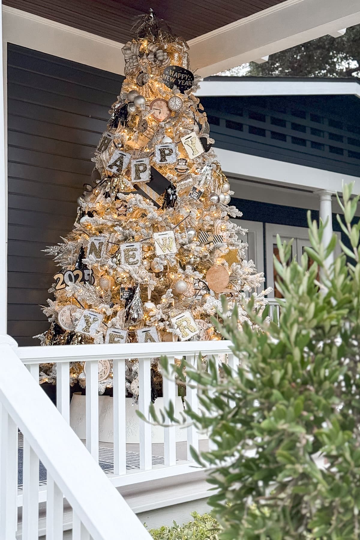 A beautifully decorated Christmas tree on a porch, adorned with ornaments, lights, and banners spelling "Happy New Year" and "2024." The tree emits a warm glow, set against a dark siding backdrop, with a white railing in the foreground.