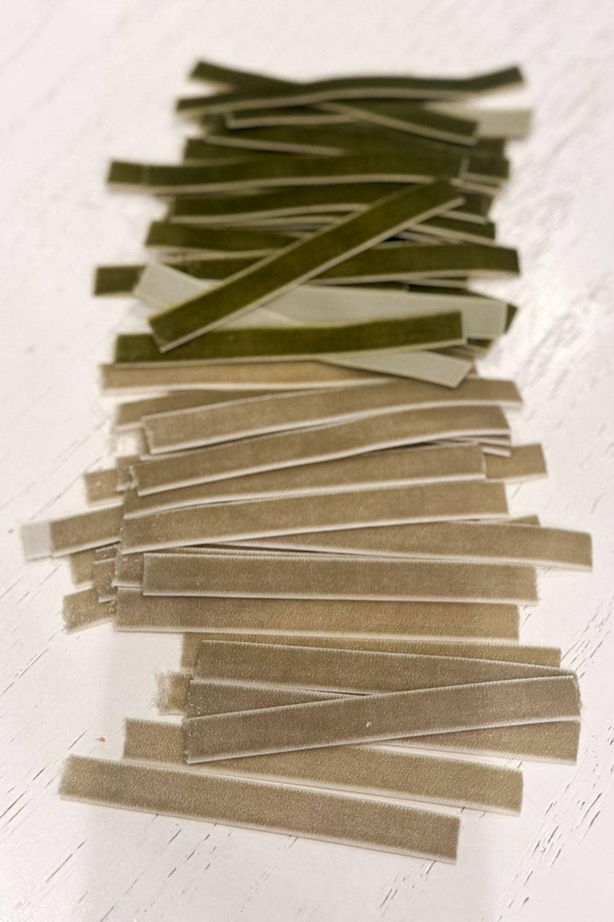 Two piles of rectangular adhesive strips, one green and one beige, are neatly aligned on a white surface. The strips have a glossy texture, and each pile forms a grid-like pattern.