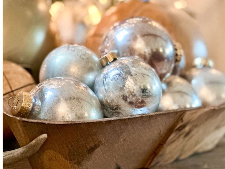 A wooden bowl filled with shiny silver Christmas ornaments, reflecting light softly. The ornaments are round with a metallic sheen, creating a festive and elegant holiday display.