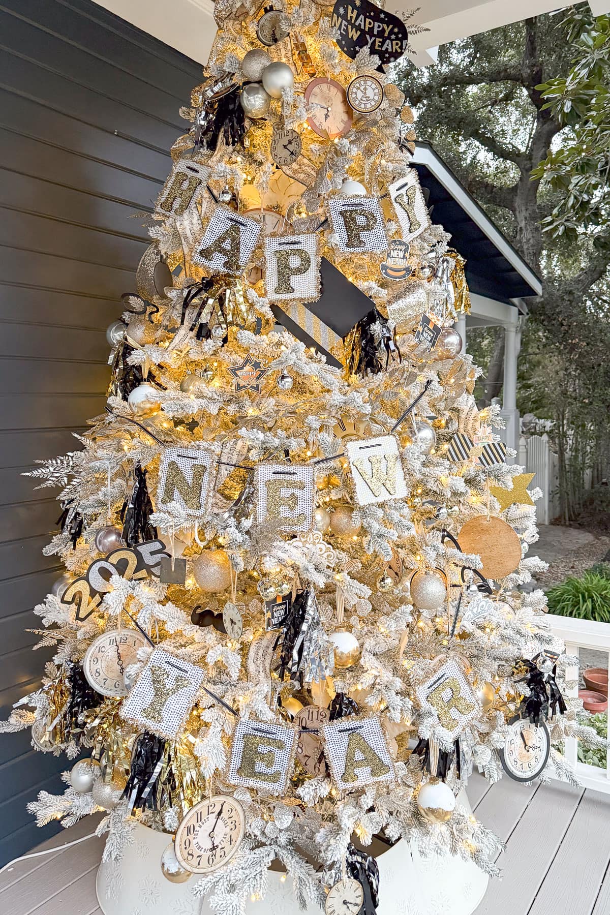 A festive New Year's tree adorned with garlands spelling "Happy New Year" in glittery letters. Decorations include clocks, stars, and a "2024" ornament, all in gold and white, with warm white lights illuminating the tree.