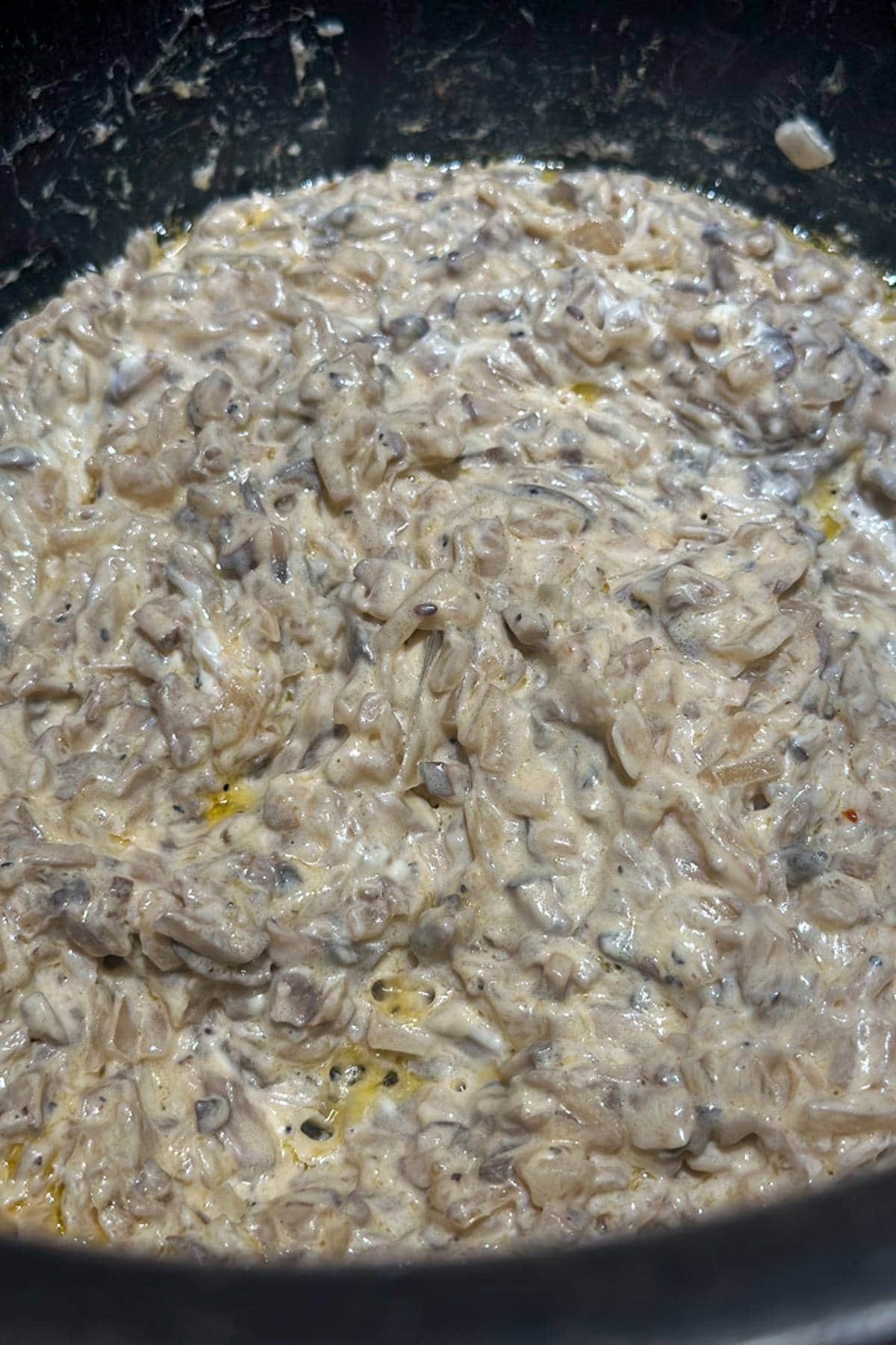 A close-up of a creamy mushroom risotto, featuring a rich mix of rice and finely chopped mushrooms cooked in a creamy sauce, with a slightly glossy surface. The dish appears warm and freshly prepared.