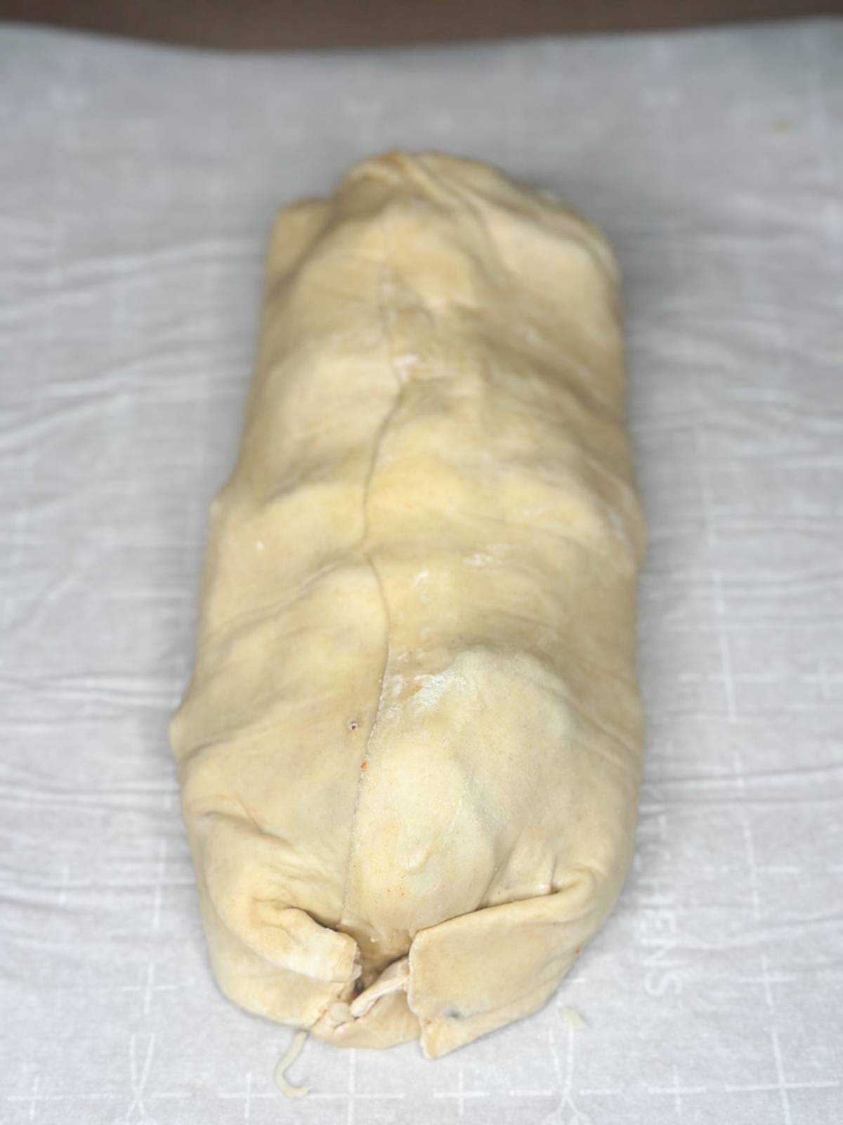 A rolled, uncooked pastry log on a sheet of parchment paper, with a light dusting of flour visible on its surface.