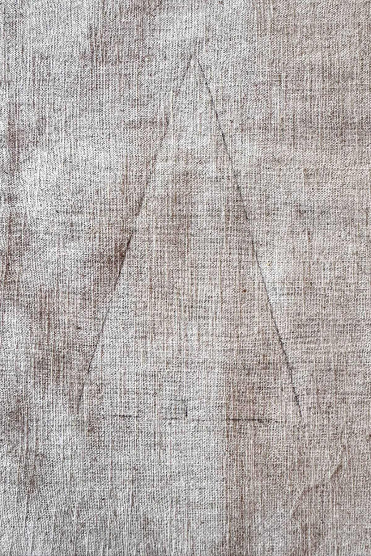 A close-up of a textured fabric surface with a faint, traced tree template  in the center. The fabric is light brown with visible fibers and subtle variations in color.