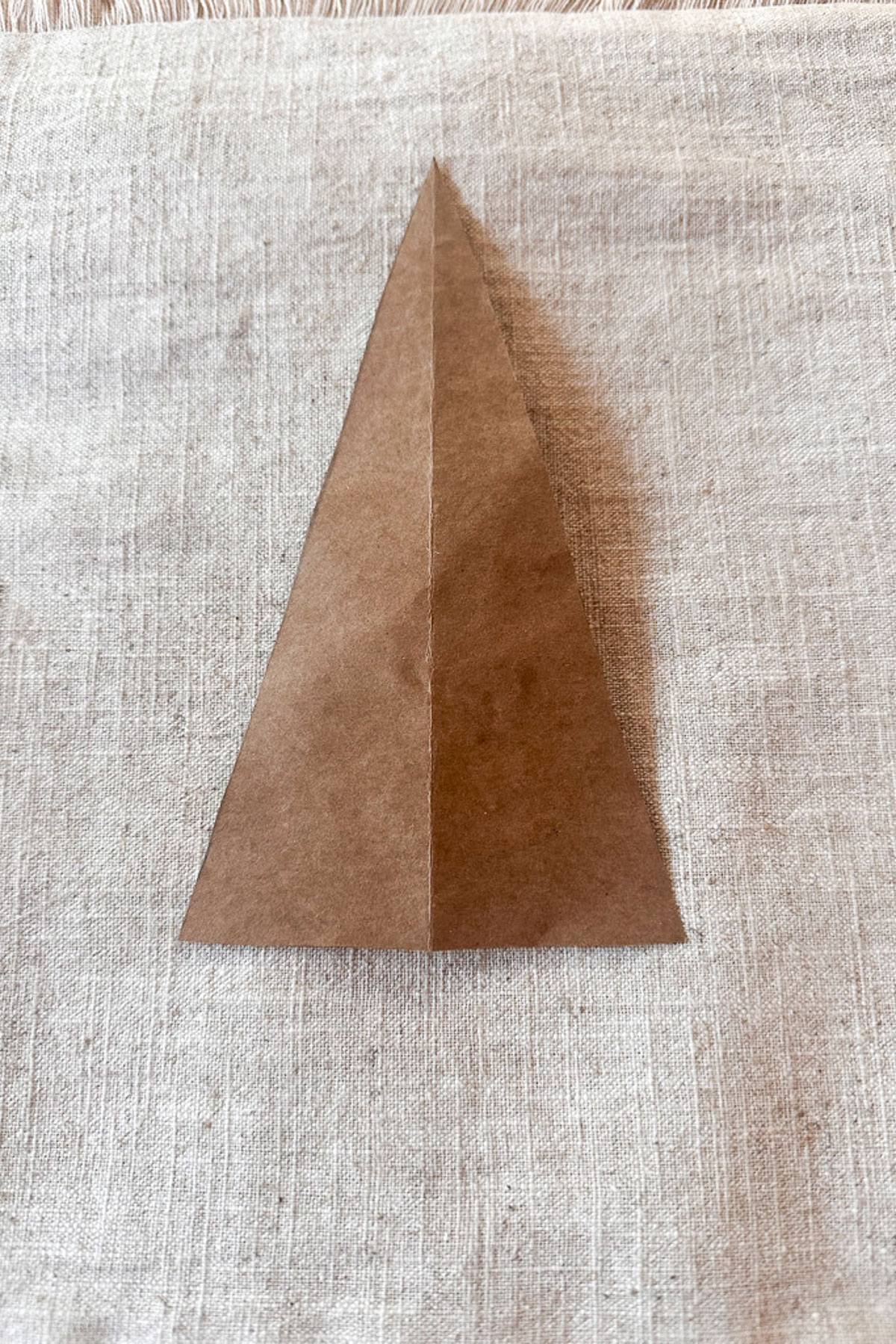 A brown paper tree template sits upright on a pillow cover. The paper is neatly folded with a central crease visible.