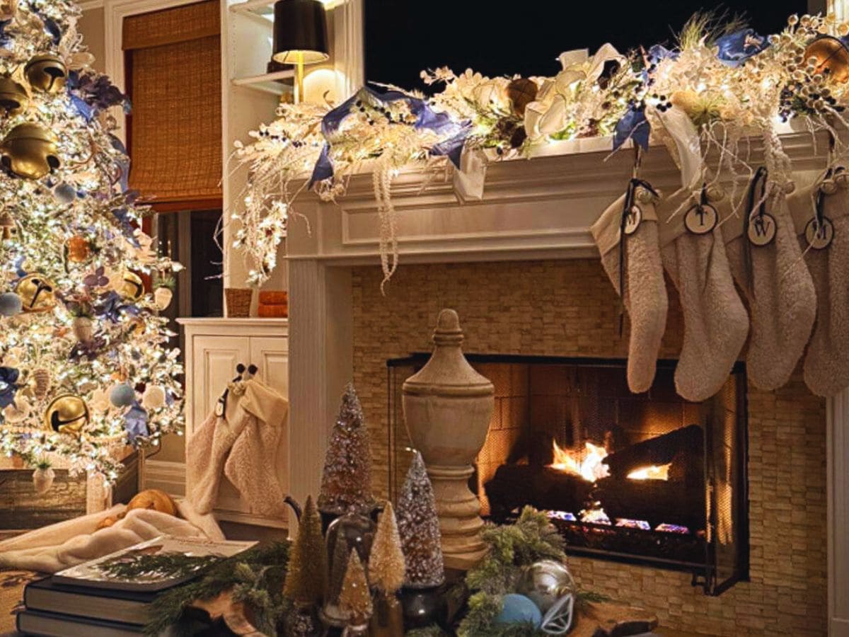 A cozy living room decorated for Christmas, featuring a lit fireplace with hanging stockings, a beautifully adorned tree with lights and baubles, and festive garlands on the mantel. Warm lighting creates a cozy, inviting atmosphere.