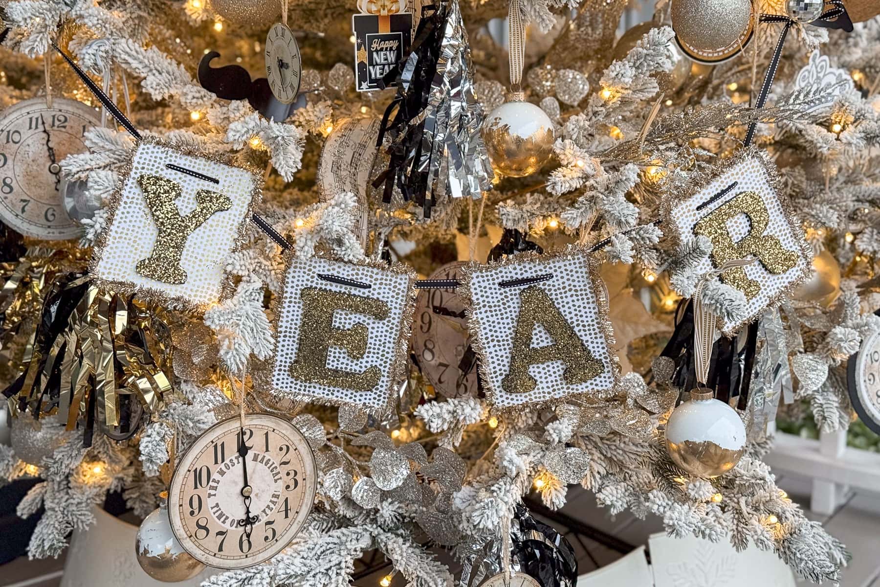 A festive New Years tree adorned with gold and white decorations, twinkling lights, and a sparkling  DIY banner spelling out "YEAR" in sequined fabric. Ornaments include glittery balls and numbers "2025.