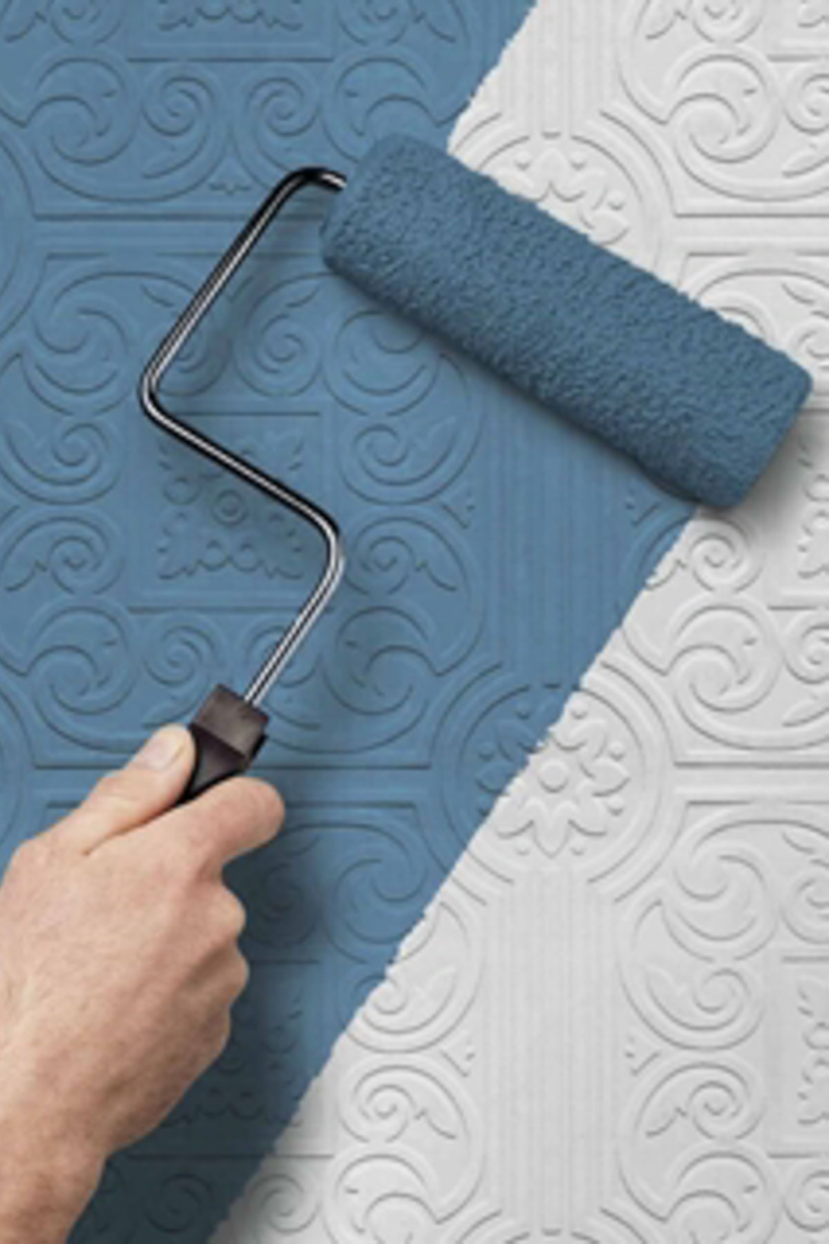 A hand with a paint roller applies blue paint over a textured, decorative white wall, updating the ornate and embossed pattern of intricate swirls and floral designs. A refreshing change transforms the space, perfect for a sophisticated dining room.