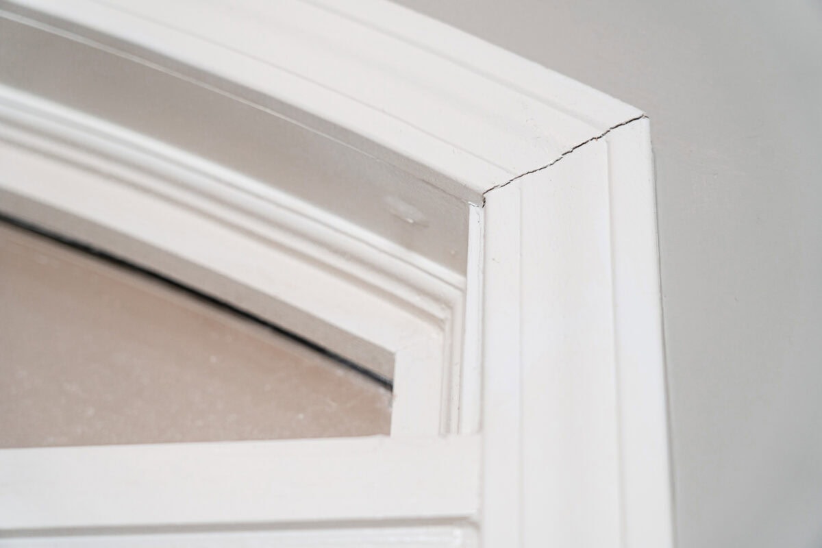 Close-up of a white-painted window frame with a visible crack in the upper corner, showing signs of wear and potential structural issues.