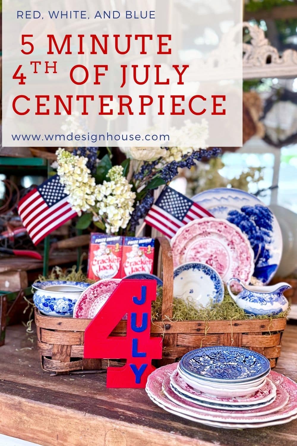 A rustic table display features a festive 4th of July basket centerpiece with red, white, and blue plates, mini American flags, a red "4 JULY" sign in a wicker basket, plus Cracker Jack boxes and flowers to complete the patriotic decor.