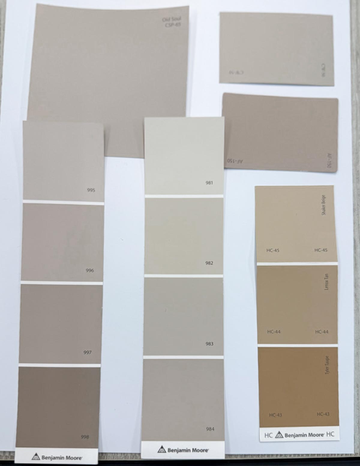 A sheet displaying various Benjamin Moore paint samples in neutral shades, including gray, beige, taupe, and tan, each labeled with different product numbers and names.
