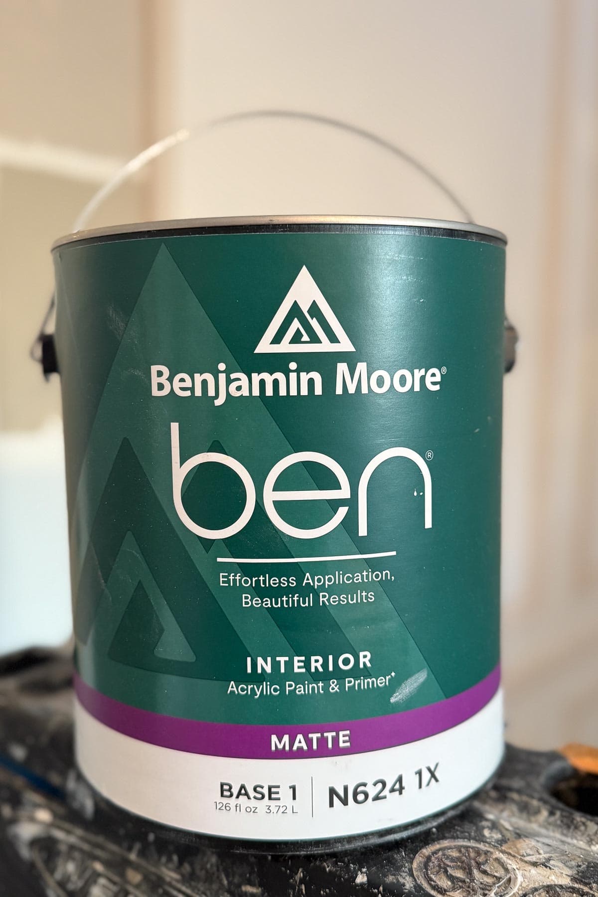 A can of Benjamin Moore ben interior matte acrylic paint and primer with a green and white label, sitting on a black surface. The label highlights "Effortless Application, Beautiful Results.