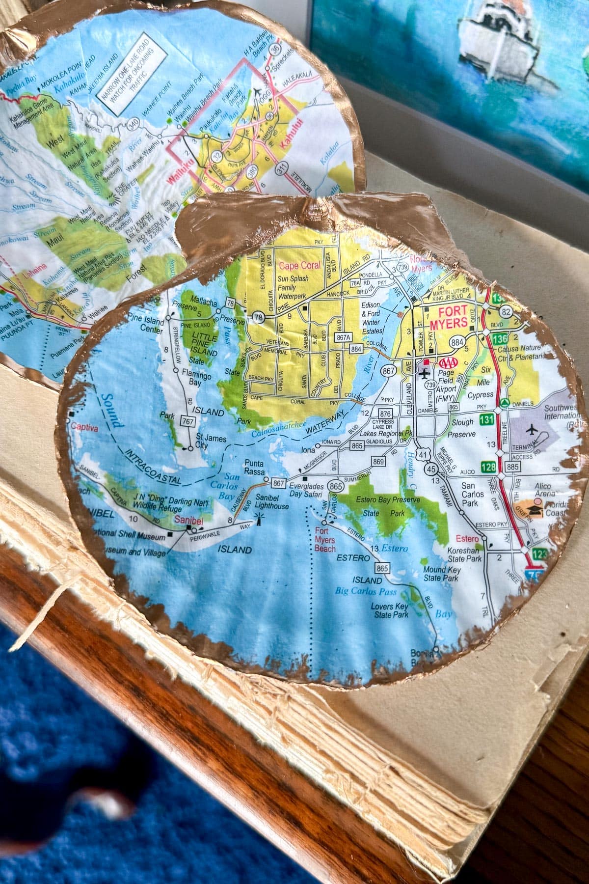 A close-up of a pumpkin-shaped cutout made from a map, featuring the Fort Myers area in Florida. The edges of the cutout are painted gold, and part of another similar cutout is visible nearby.