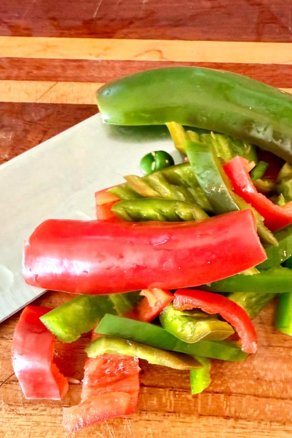Sliced red and green bell peppers on a cutting board with a large knife.
