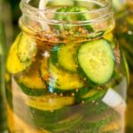 A close-up of a glass jar filled with sliced cucumbers, onions, and spices soaking in a pickling liquid, ready to make homemade pickles.