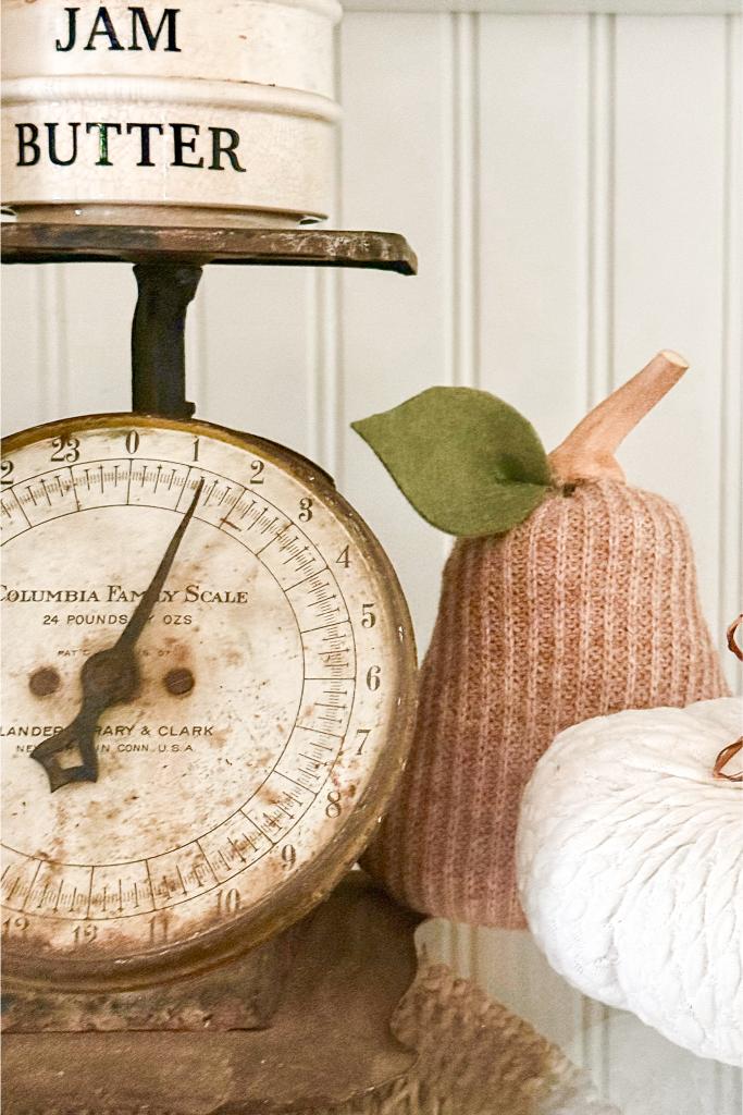 DIY Sweater Pears-A vintage Columbia Family Scale sits next to a knitted pink pear with a felt leaf and a white textured pumpkin. Two stacked tins labeled "JAM" and "BUTTER" rest on top of the scale.