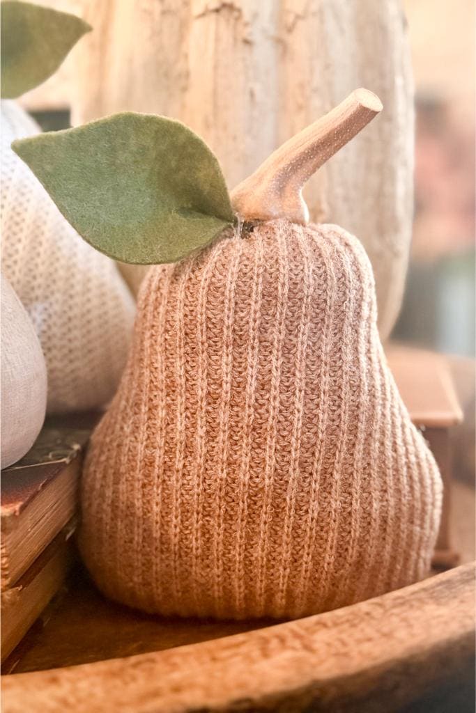 A knitted fabric pear with a felt leaf and wooden stem sits on a wooden tray, creating a cozy, rustic decor scene.