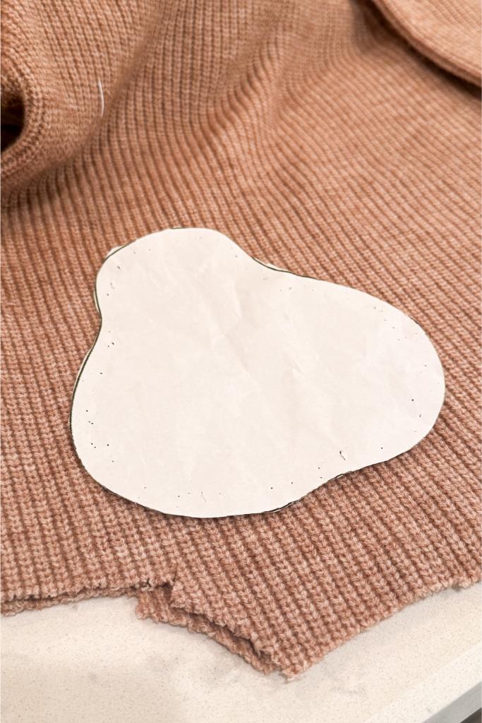 Sweater pear - A roughly cut piece of white paper shaped like an irregular blob is placed on a brown ribbed fabric with a torn edge, possibly for use as a pattern or template.