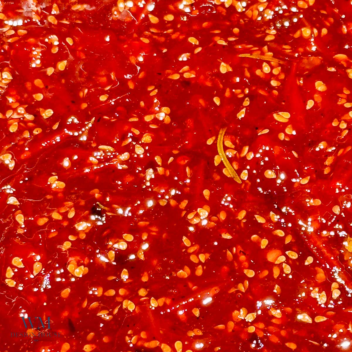 Close-up of a bright red tomato jam with visible seeds and small rosemary pieces, creating a textured and glossy appearance reminiscent of tomato jam.