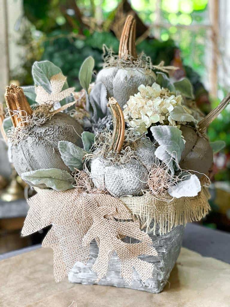 A rustic arrangement featuring fabric pumpkins, dried hydrangeas, artificial leaves, and natural moss in a textured pot—this charming autumn centerpiece is perfect for showcasing your love of pumpkin crafts.