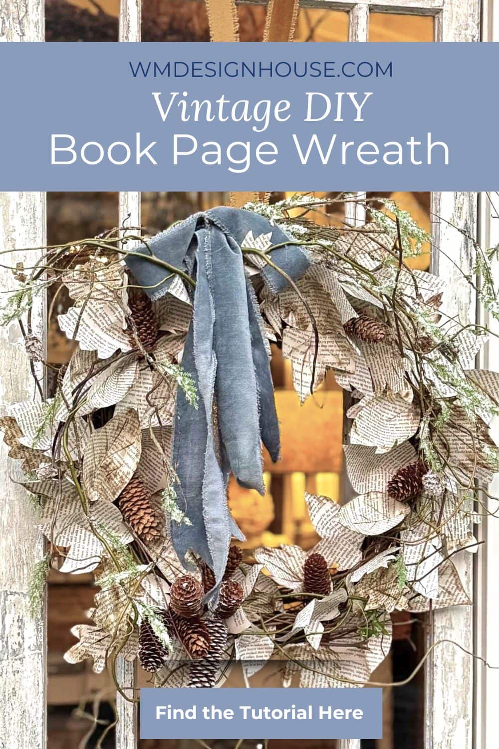 A decorative book page wreath made from book pages, pinecones, and leaves, accented with a blue velvet ribbon, hangs on a rustic white door. Text above reads, "Vintage DIY Book Page Wreath" and "Find the Tutorial Here.