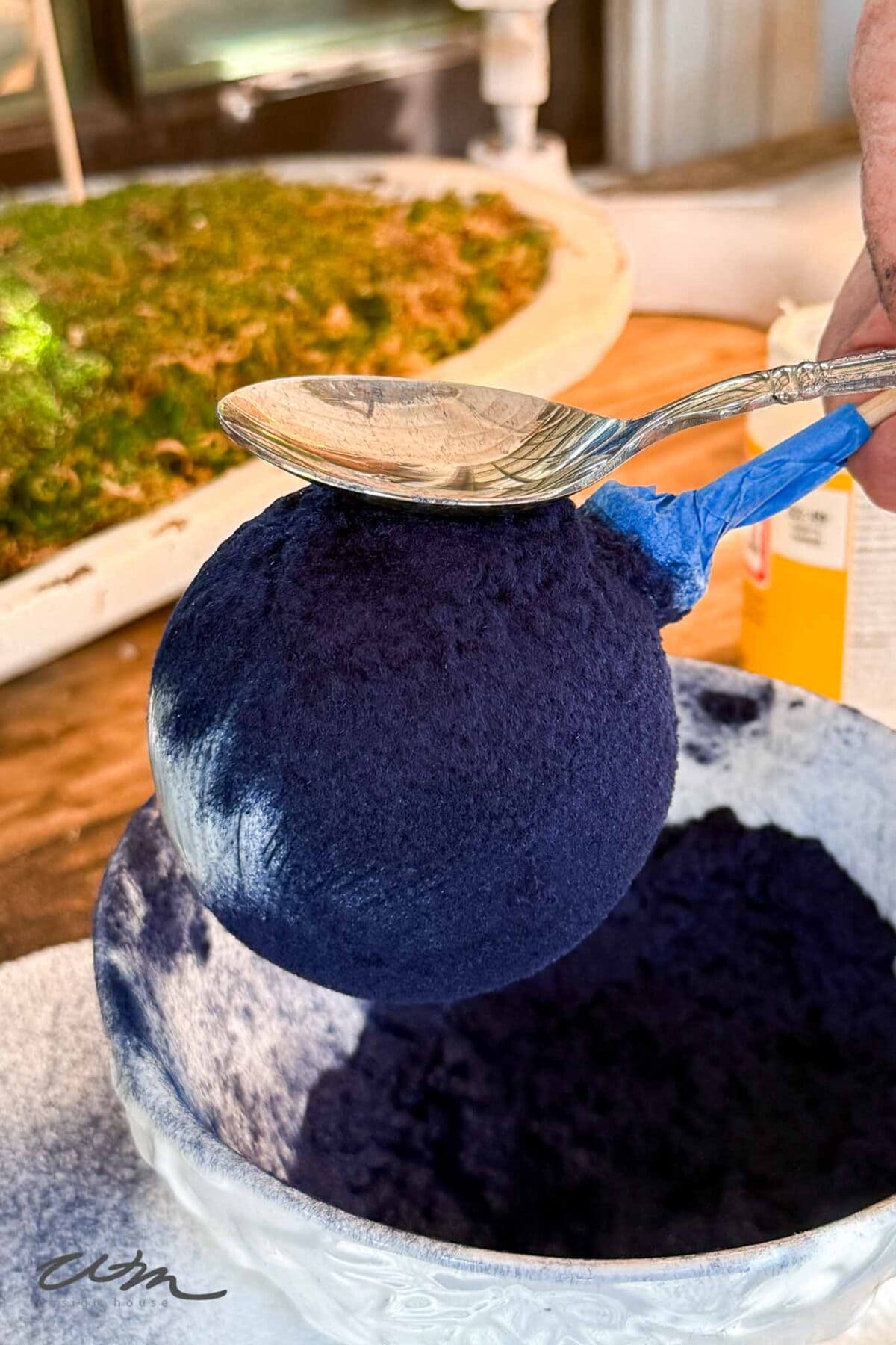 A person holding a spoon over a round ball of blue paint.