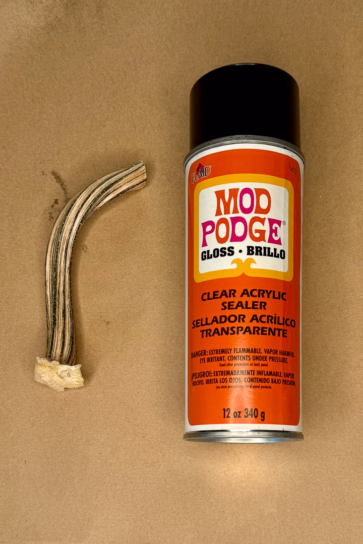 A bundle of antler pieces bound with tape lies next to a can of Mod Podge Gloss Clear Acrylic Sealer on a brown surface.