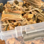 A clear plastic container filled with dried okra pieces, showing their ridged, brownish exterior and rough, textured surfaces.