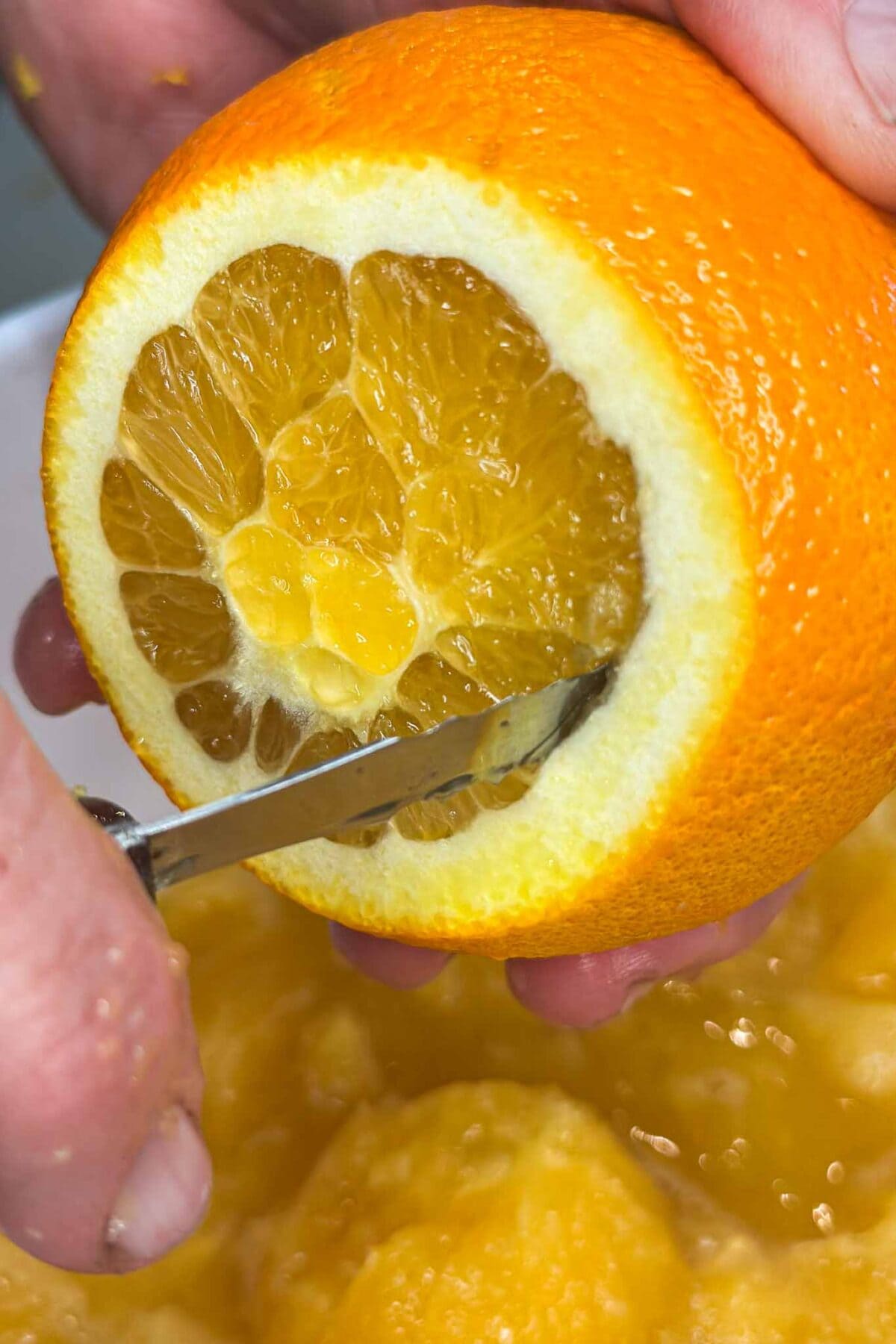 A close-up of hands using a knife to cut into an orange, with the peel partially removed and visible juicy orange segments inside.