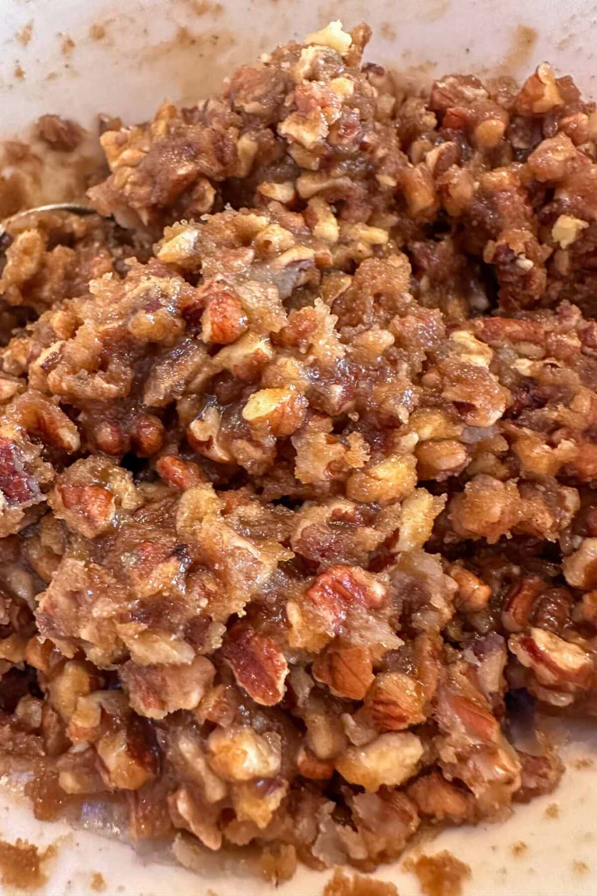 A close-up of a crumbly mixture containing chopped nuts, brown sugar, and oats, combined in a bowl, resembling a dessert topping or streusel before baking.