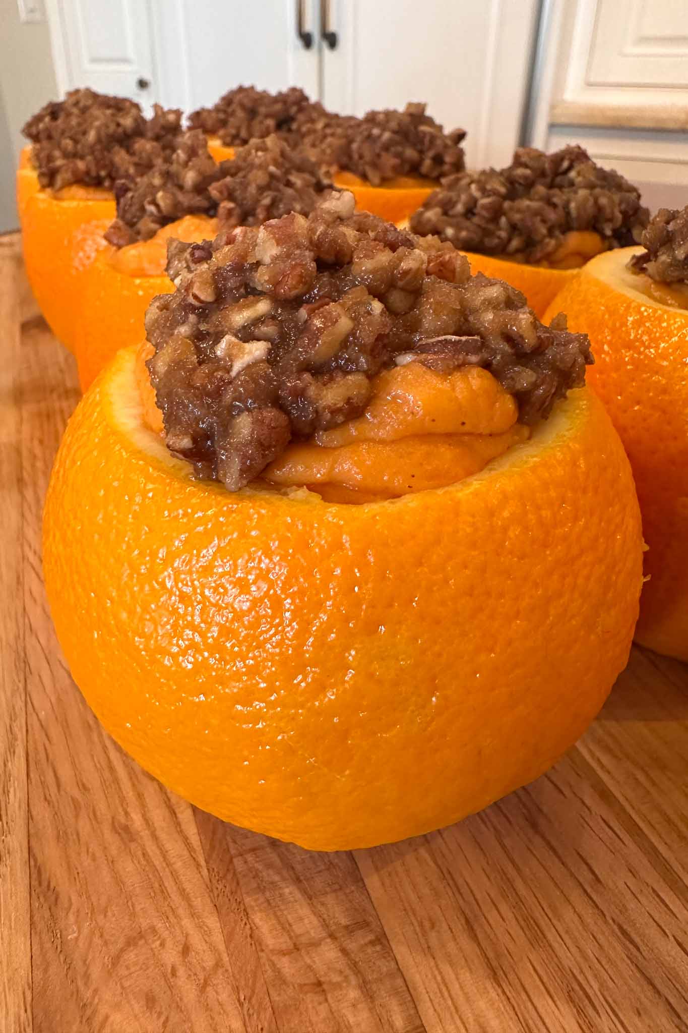 Hollowed-out oranges filled with a sweet, brown, nutty mixture are arranged on a wooden surface in a kitchen.