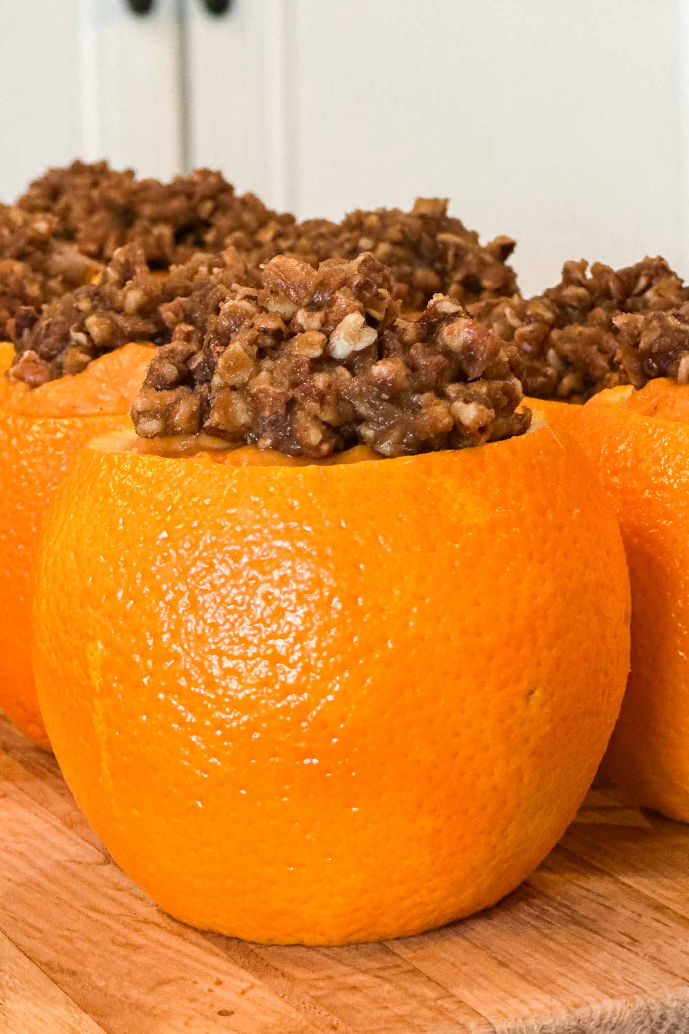 Several oranges with their tops cut off are filled with a chunky brown mixture, possibly a dessert or baked filling, and are arranged on a wooden surface.